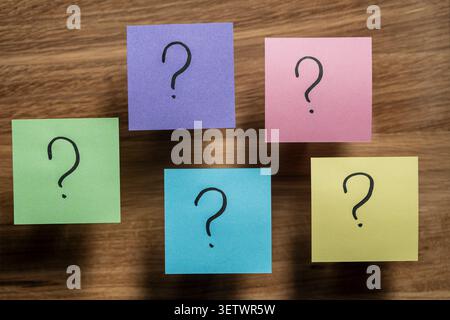 Sticky notes with question marks on wood background. Five multicolored papers with handwritten question marks. Conceptual image for choices Stock Photo