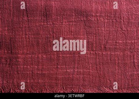 Textured dark red linen fabric background with fringe. Close up of burgundy woven textile material texture with fringed edge. Perfect for rustic desig Stock Photo