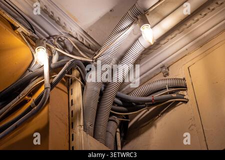 Exposed electrical conduits and bulbs in ceiling corner. Ceiling corner with exposed corrugated electrical conduits, cables, pipes, and glowing bulbs Stock Photo