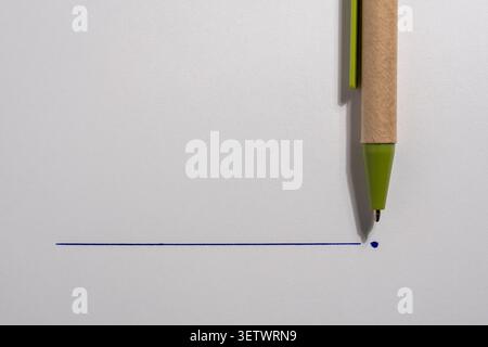 Eco friendly paper pen drawing a blue line on white background. Close up of a recycled cardboard pen with green plastic details drawing a straight blu Stock Photo