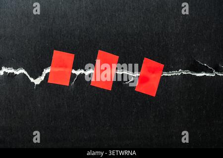 Torn black paper fixed with red adhesive tape concept, close up. Torn dark cardboard sheet repaired with three pieces of red electrical tape concept o Stock Photo