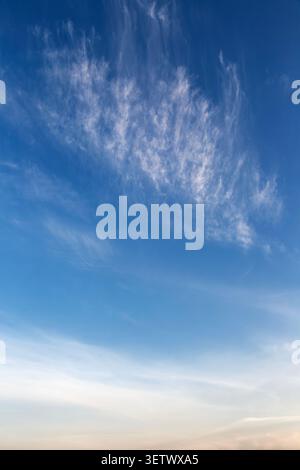 Wispy cirrus clouds on blue sky with golden sunset glow at the horizon. Stock Photo