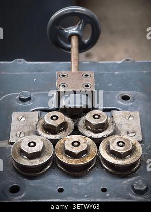 Worn industrial roller assembly with multiple metal rollers, hex nuts, washers, and mounting plates fixed to painted machinery base, showing grease, r Stock Photo