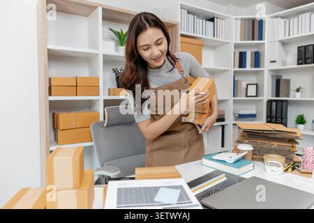 Small business owner preparing customer orders by packing boxes, checking products, recording shipment details and managing online sales in a home off Stock Photo