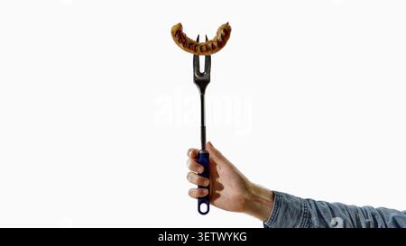 Hand holding grilled sausage on long fork over white background. Stock Photo