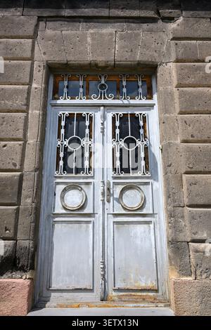 Weathered double door with ornate metalwork. Stone wall surrounds the entrance. Rusty hinges and peeling paint visible Stock Photo