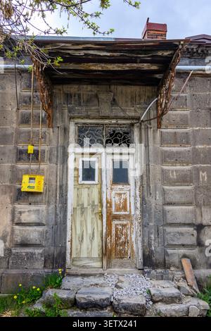 Old weathered door with peeling paint on stone house. Rusty metal roof overhangs doorway. Yellow mailbox hangs beside entrance. Moss and weeds grow ne Stock Photo