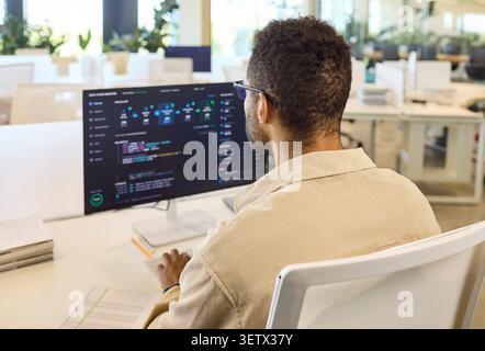 Male programmer coding at desktop computer in bright modern office workspace Stock Photo