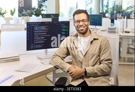 Confident software developer smiling at monitor with source code in bright office Stock Photo