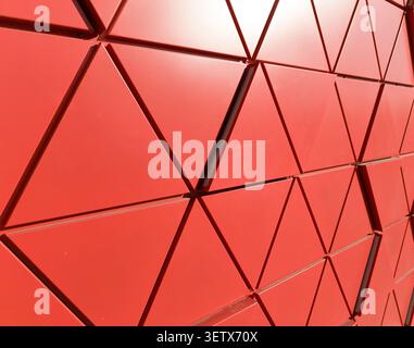 Red geometric facade with triangular panels forming dynamic architectural pattern. Surface structure creates depth and bold composition. Concept of mo Stock Photo