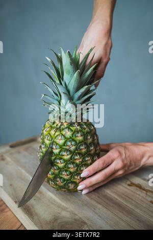 Hands cut a pineapple on a wooden board in a kitchen setting during the day Stock Photo