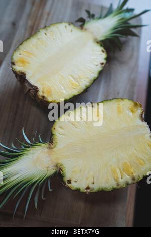 Fresh pineapple cut in half on wooden surface showing yellow flesh and green crown Stock Photo