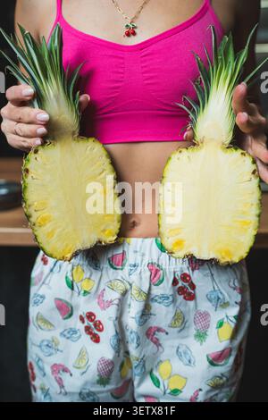 Woman holds a halved pineapple in a kitchen while wearing casual clothes Stock Photo