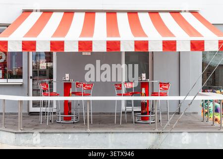 Outdoor cafe terrace equipped with a large red and white striped awning, characteristic of a classic bistro style Stock Photo