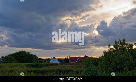 Sunset light breaking through dark storm clouds over a rural village and fields Stock Photo