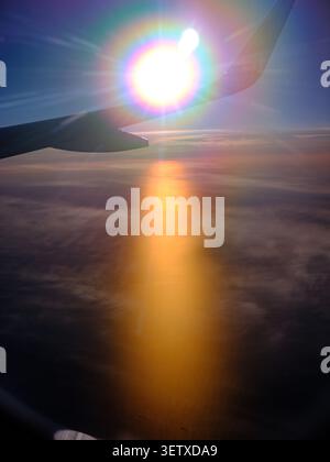 A view from plane window of a dramatic Sun set over Sweden during the midnight sun over the wing of the plane flaring rainbow colours into the camera Stock Photo