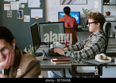Adult Man Coding at Dual Monitors in Modern Office Workspace Stock Photo