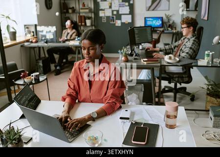 Black Woman Working on Laptop in Creative Office Team Setting Stock Photo