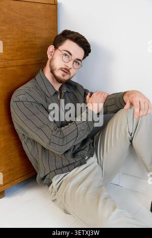 Charming young man with beard poses thoughtfully in a studio with wooden backdrop Stock Photo
