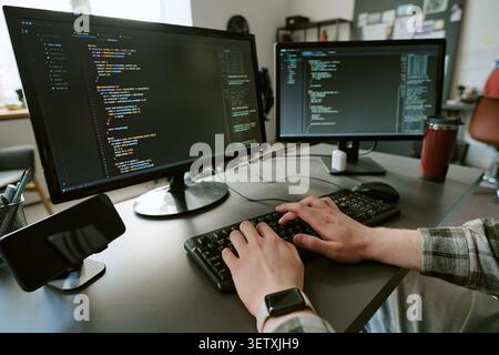Adult Man Typing Code on Dual Monitors in Software Development Stock Photo
