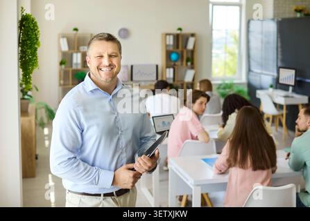 Smiling teacher with tablet leading adult students in modern classroom setting Stock Photo