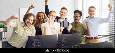 Happy diverse developers team cheering in office after coding project success Stock Photo