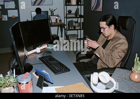 Asian Man Checking Smartphone during Late Night Office Work Stock Photo