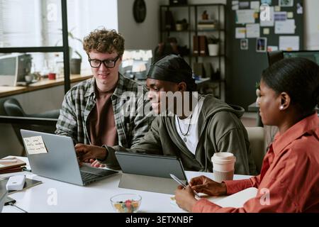 Diverse Colleagues Collaborating on Laptop in Creative Workspace Stock Photo