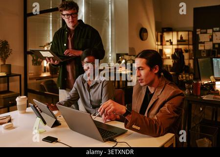 Diverse Coworkers Reviewing Laptop Data during Evening Office Meeting Stock Photo