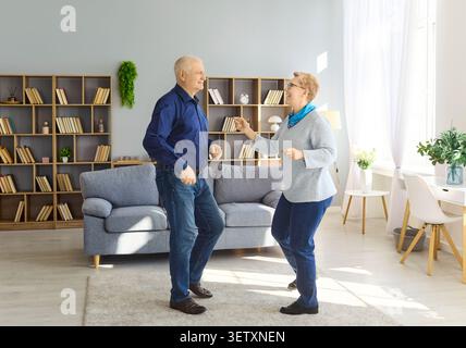 Senior couple dancing together at home in bright living room, joyful retirement Stock Photo