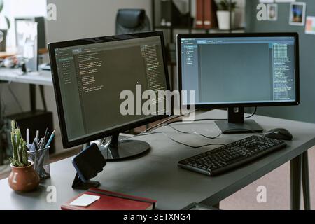 Dual Monitors Displaying Software Code in Modern Office Workspace Stock Photo