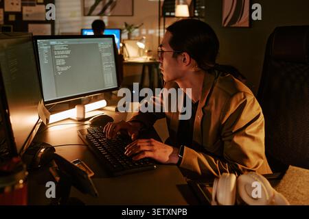 Asian Man Coding at Computer during Night Shift in Office Stock Photo
