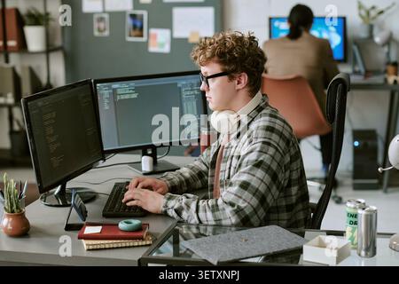 Man Typing Code at Dual Monitors in Shared Office Stock Photo