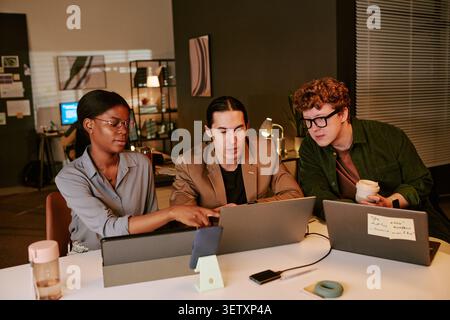 Diverse Coworkers Reviewing Laptop Data during Late Office Meeting Stock Photo