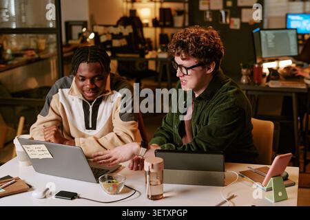 Black Man and Man Collaborating on Laptop in Creative Office Stock Photo