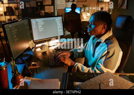 Black Man Coding at Dual Monitors in Night Software Office Stock Photo