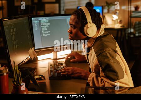 Black Man Coding at Dual Monitors in Office at Night Stock Photo