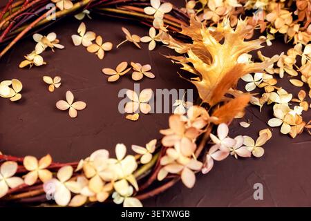 autumn wreath from grape branches, dried hydrangea flowers and oak leaves on brown background. Grape vine wreath. Stock Photo