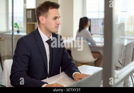 Focused businessman working at computer in office, coworker in background Stock Photo
