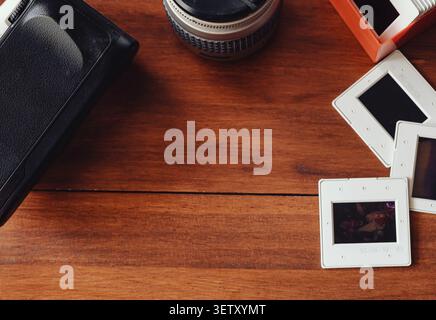 A nostalgic composition on a wooden table featuring vintage slides, an antique lens, and analog photography equipment. Stock Photo