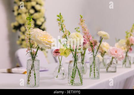Fresh flowers arranged in clear glass vases on table during an event with elegant setup. Stock Photo