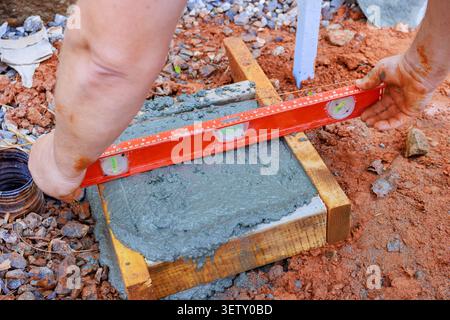 Construction worker levels freshly poured concrete in wooden form at building site Stock Photo