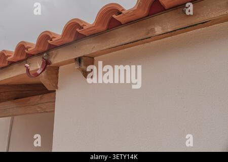 Low angle view of a ceramic tile roof edge with an empty metal bracket on a stained wooden beam, where the drainage gutter has completely fallen off d Stock Photo