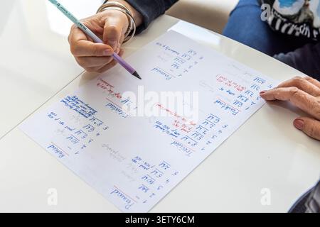 Close-up of hands reviewing and writing notes on a planning sheet during a meeting, highlighting teamwork and project management. Stock Photo