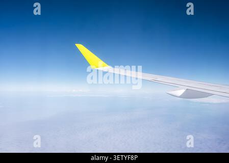 Aerial passenger window view of yellow wingtip above soft clouds Stock Photo