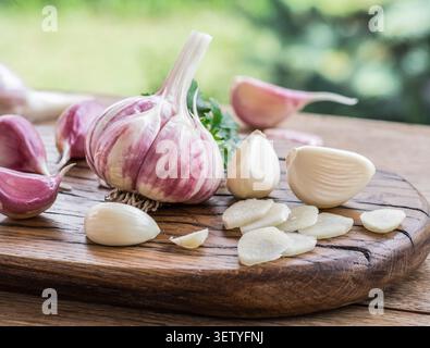Fresh garlic bulbs with several cloves and sprigs of green parsley  on a wooden table on a nature rural background. This vibrant image ideal for cooki Stock Photo