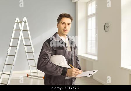 Builder inspector with clipboard and helmet making notes during room renovation Stock Photo
