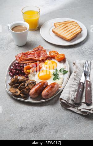 Full English breakfast served on a plate with fried eggs, crispy bacon, grilled sausages, mushrooms, beans, tomatoes, toasts, coffee and orange juice. Stock Photo