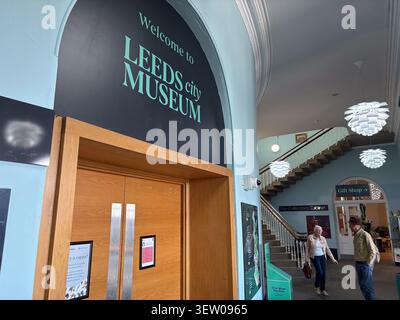 Interior view of the entrance at Leeds City Museum in Leeds, West Yorkshire, England, featuring museum signage and visitors near a staircase. Stock Photo