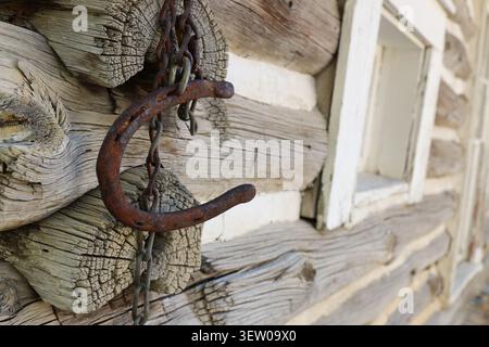 Rusty horseshoe hanging from a chain on the weathered log wall of a historic cabin in Helena, Montana, USA. Stock Photo